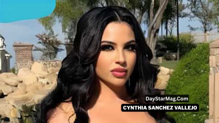 A woman with long black wavy hair poses outdoors in bright sunlight, with stone structures, greenery, and trees in the background. She has bold makeup and a serious expression. A black label on the lower right displays the text “DayStarMag.com” and “CYNTHIA SANCHEZ VALLEJO.”