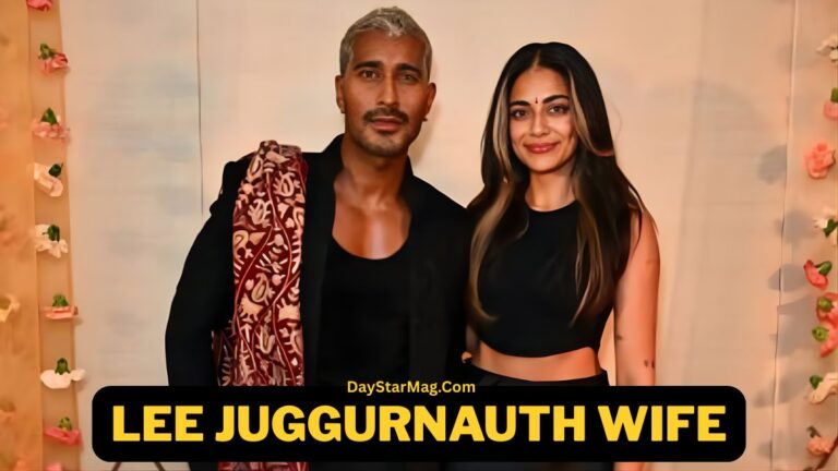 A man and a woman standing together and posing for a photo in front of a softly decorated backdrop with small flowers. The man is wearing a dark outfit with a patterned shawl, and the woman is wearing a black sleeveless top and smiling. Text at the bottom reads “Lee Juggurnauth Wife – DayStarMag.com.”