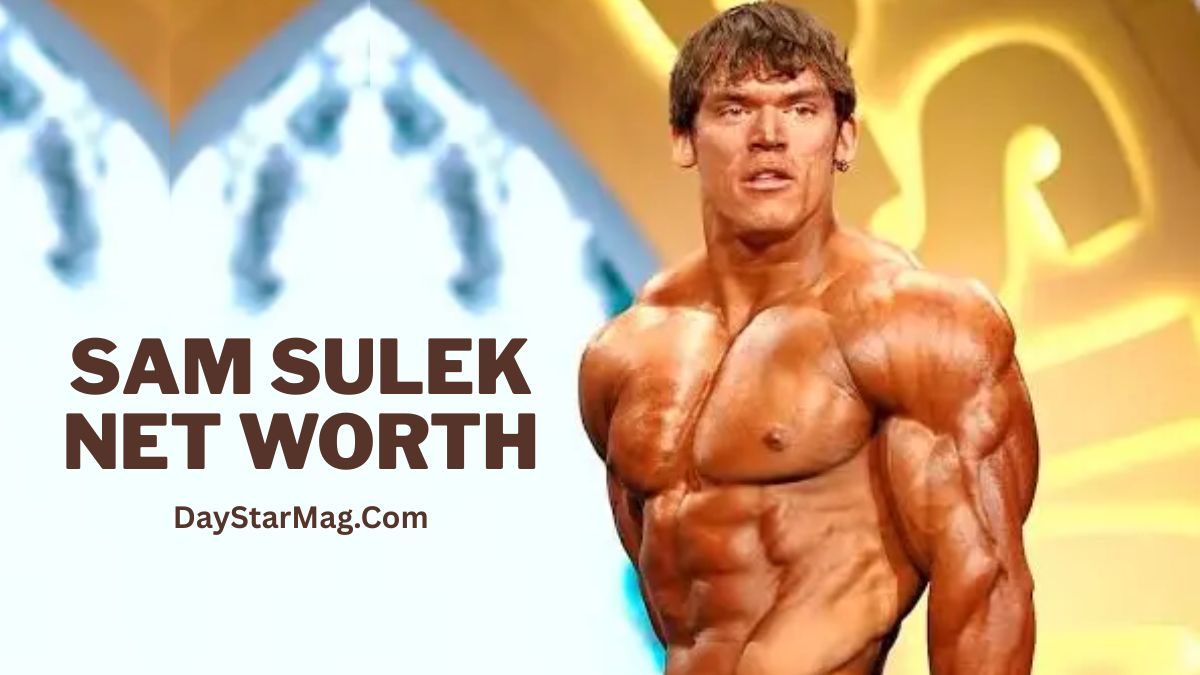 Muscular male bodybuilder posing shirtless on a stage under bright lights, with defined chest and arm muscles visible. Text on the image reads “sam sulek net worth” and includes the DayStarMag.com branding.